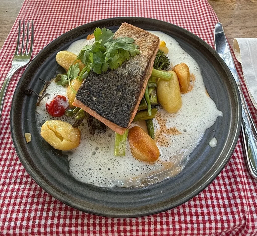 Knuspriges Lachsfilet mit Haut auf cremiger Sauce, dazu Gnocchi, grüner Spargel und Kräuter, serviert in einem Schwarzwald-Restaurant.