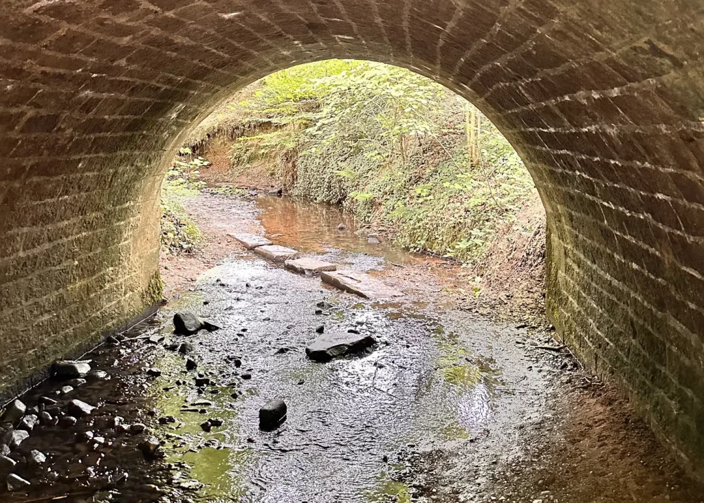 Bachlauf durch eine kleine Tunnel-Unterführung im Sulzbachtal